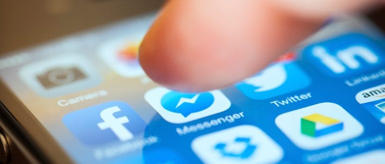 A smartphone displaying social media icons. A person's finger moves towards one of the icons.