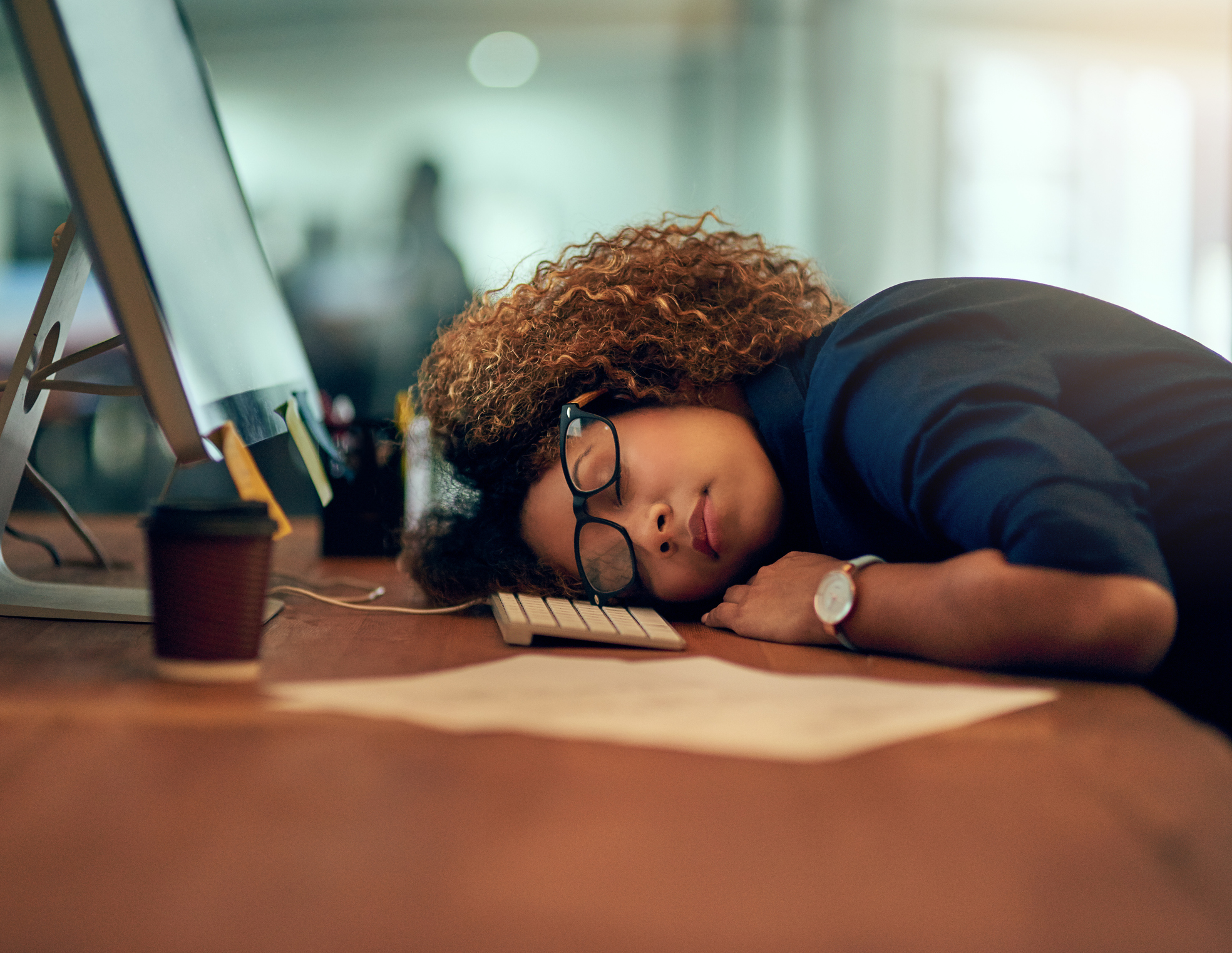 A woman sitting at a desk sleeps with her head on a keyboard.