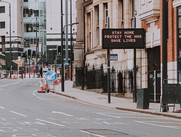 An empty city street. An electronic traffic sign states: Stay Home. Protect the N H S. Save Lives.