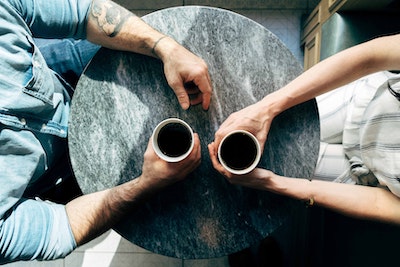 A photograph from above of two people sitting at a table, each holding a drink.