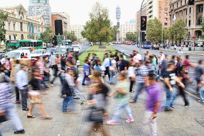 A blurred photograph of a group of people walking on a crosswalk in a city.