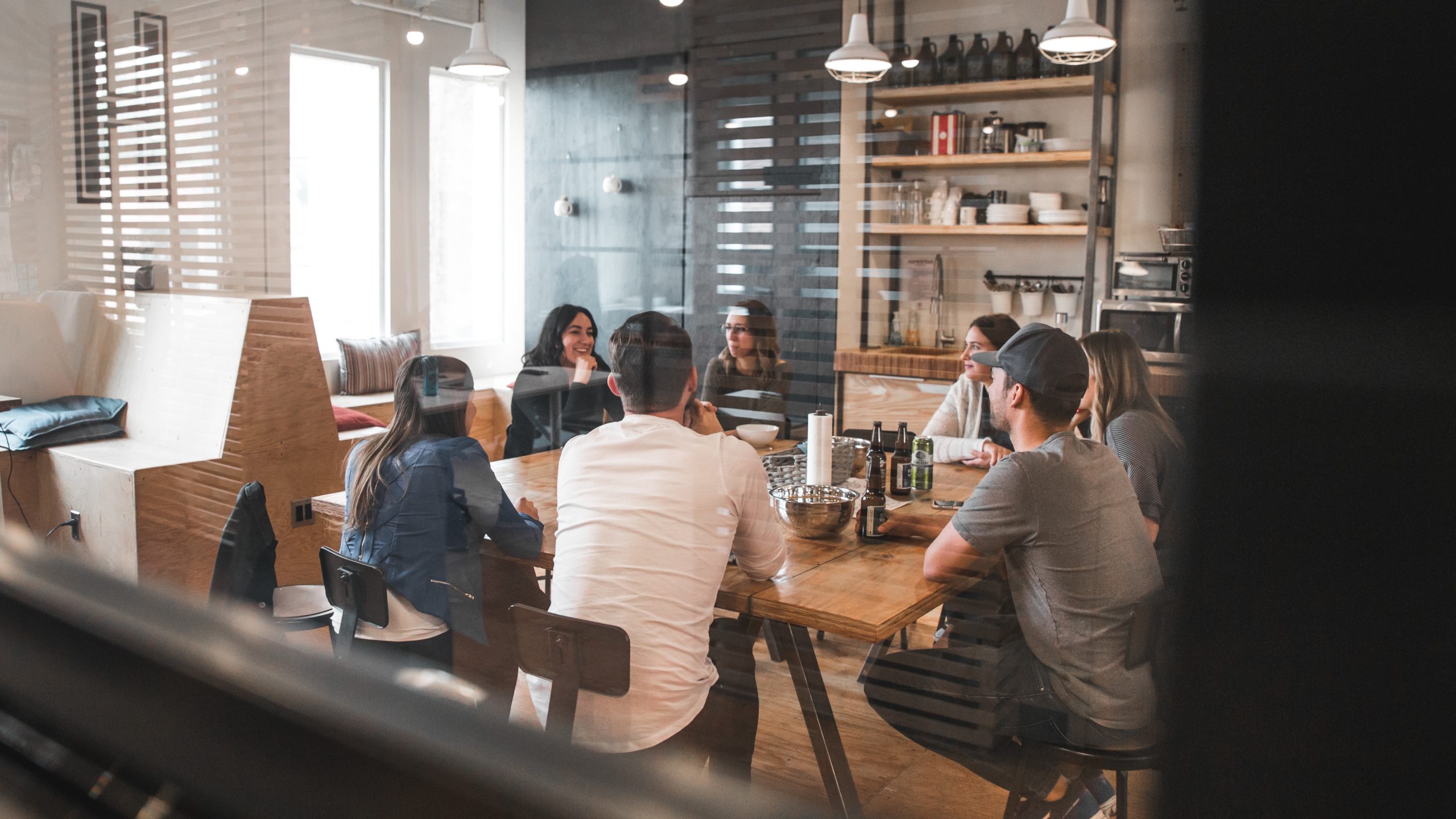 A group of people sit around a large table. Drinks are on the table.